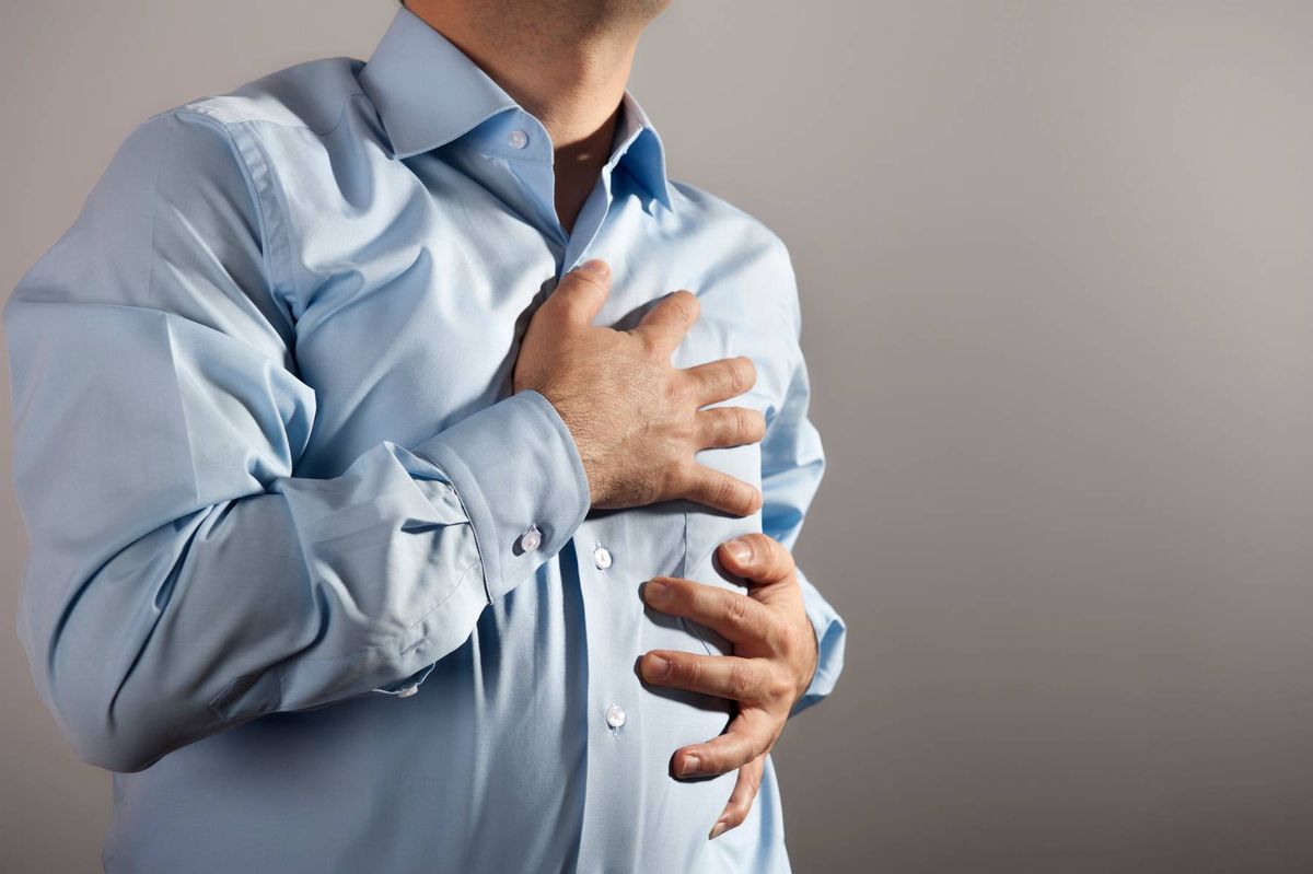 Young man clutching his chest in pain wearing a blue shirt