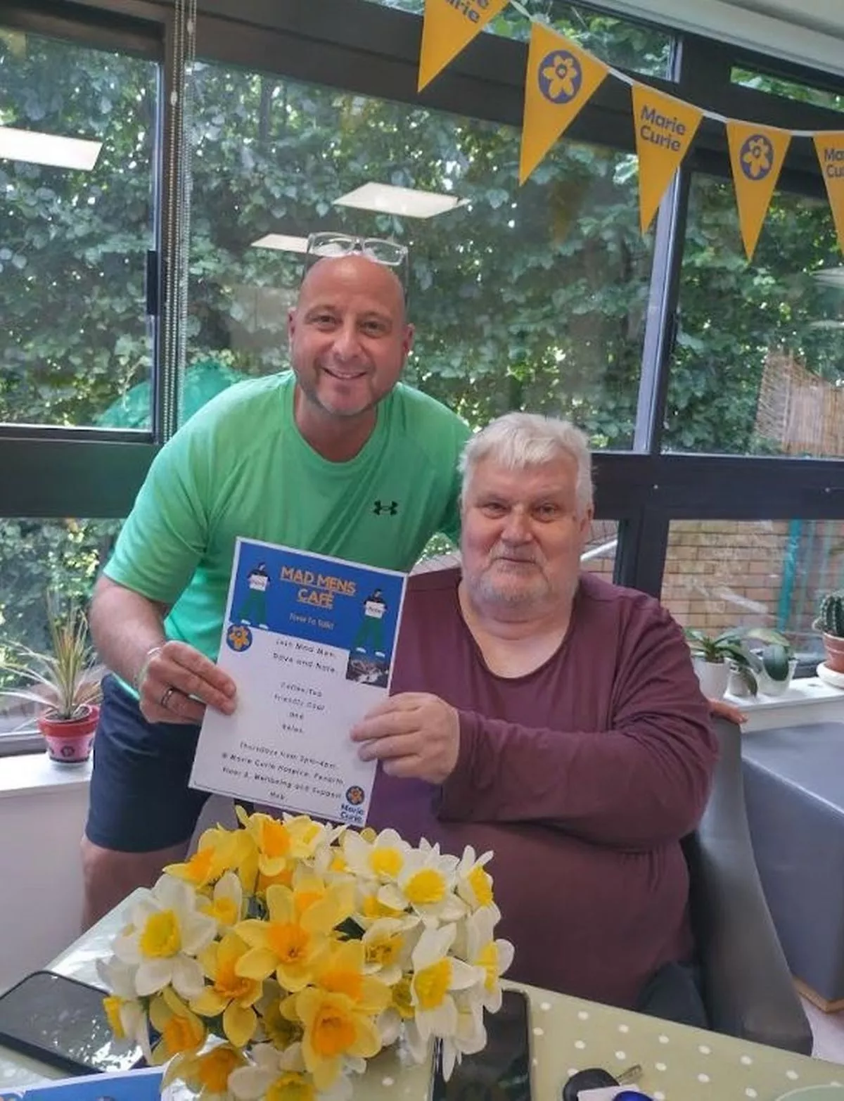 A young bald man next to an older gentleman with grey hair who is sat in a wheelchair