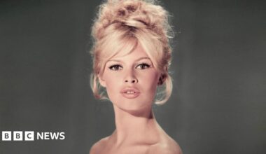 A studio portrait of Brigitte Bardot wearing a light blue off-the-shoulder dress with a blonde beehive hairdo and her lips slightly parted in a pout.