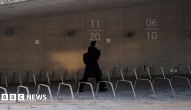 A young woman wearing a full black outfit talking on her phone as she walks