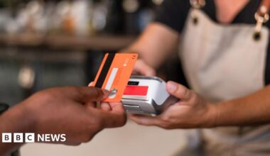 Contactless card payment being made with a card held in a hand and a terminal being held by someone in an apron.