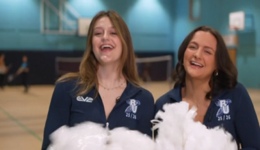 Eve Kimberley (left) and Liv Teague are wearing dark blue cheerleaders outfits and waving pompoms in a gym.
