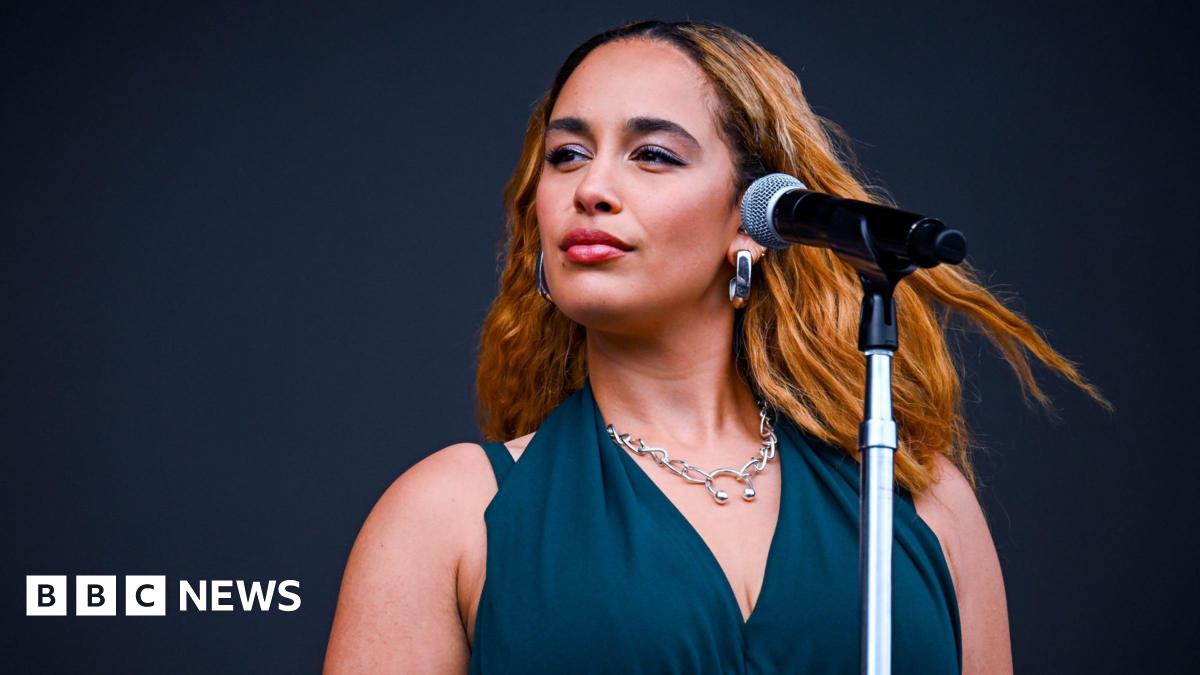 Claire Corkery, a woman with long hair, wearing a beige jumper and a gold necklace, standing in her dining room.