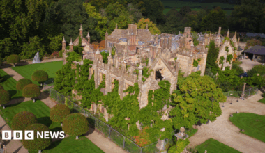 An aerial view of Parnham House. Trees and shrubs are growing out through windows as well as up through the interior of the turreted building, which has no roof in places. By contrast, the surrounding parkland is immaculately landscaped.