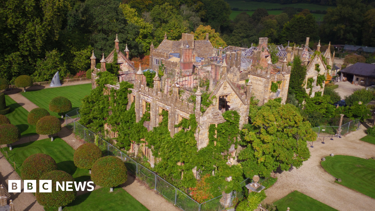 An aerial view of Parnham House. Trees and shrubs are growing out through windows as well as up through the interior of the turreted building, which has no roof in places. By contrast, the surrounding parkland is immaculately landscaped.