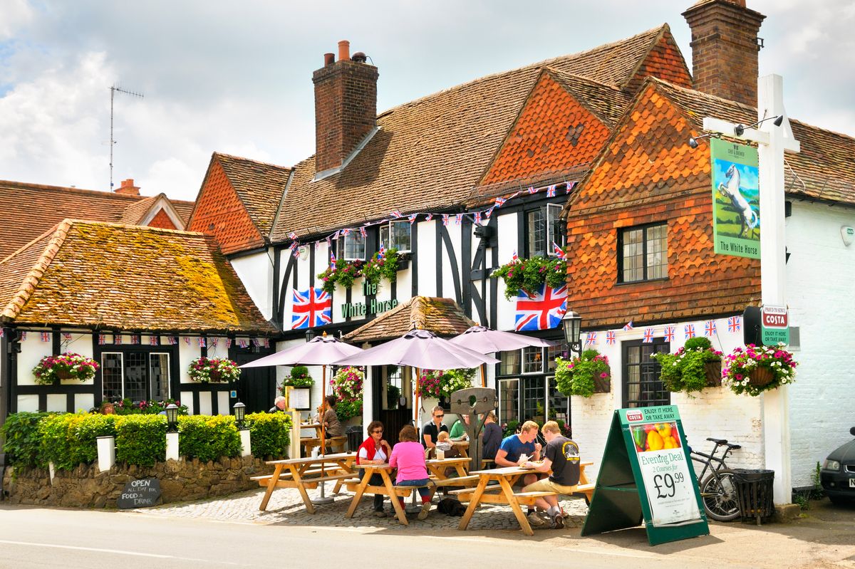 People sitting outside in summer enjoying food and drinks at the White Horse Inn, a traditional 15th-century pub in the picturesque village of Shere in Surrey, England, UK. 