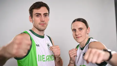 Sportsfile / Getty A man and a woman are pictured holding their fists in a boxing pose for a promotional image. They are both dressed in sleeveless green and white Team Ireland tops with the word 'IRELAND' on the chest.