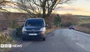 Two vehicles parked on the sides of a dry stone wall-lined rural road