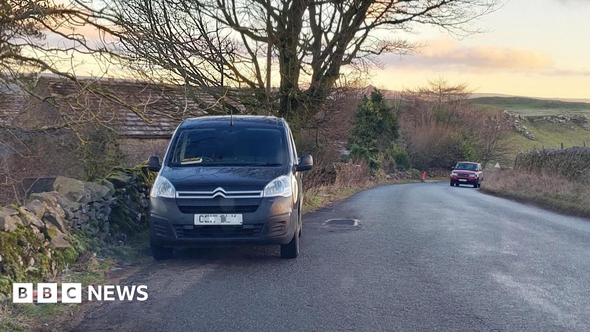 Two vehicles parked on the sides of a dry stone wall-lined rural road