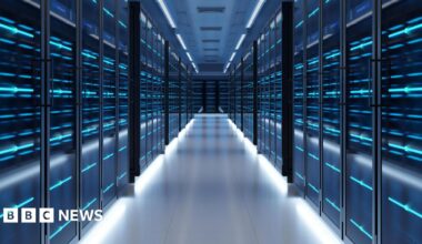 A view of a data centre corridor lined with dark cabinets covered in lights. The mood is sinister.