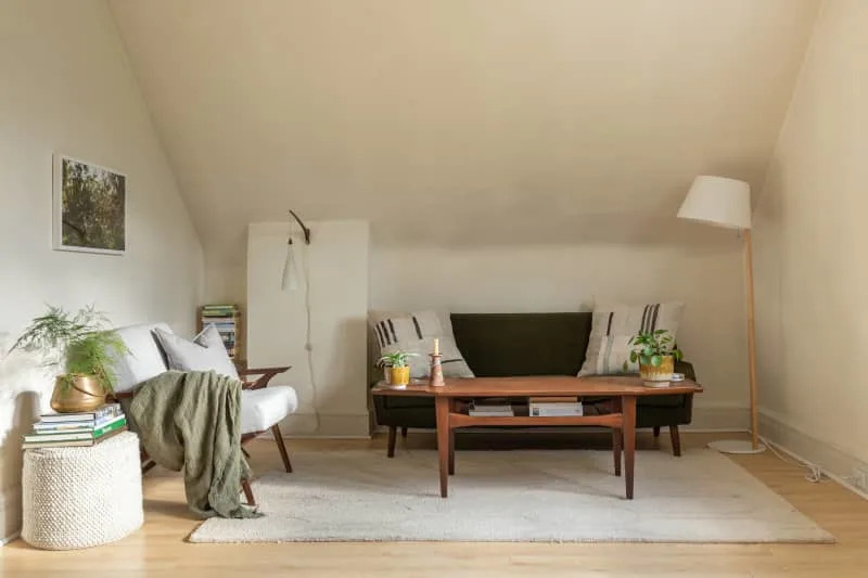 Cozy living room with a green sofa, wooden coffee table, white armchair, and potted plants on a light rug.