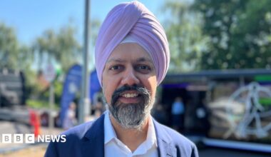 Slough MP Tan Dhesi is wearing a pink turban as well as a white shirt and navy suit. He is smiling and the pop-up heart clinic is visible in the background.