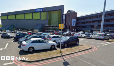 Cars parked in a car park. A building is behind it with the words Odeon and yellow mall. A car park building is to the right.
