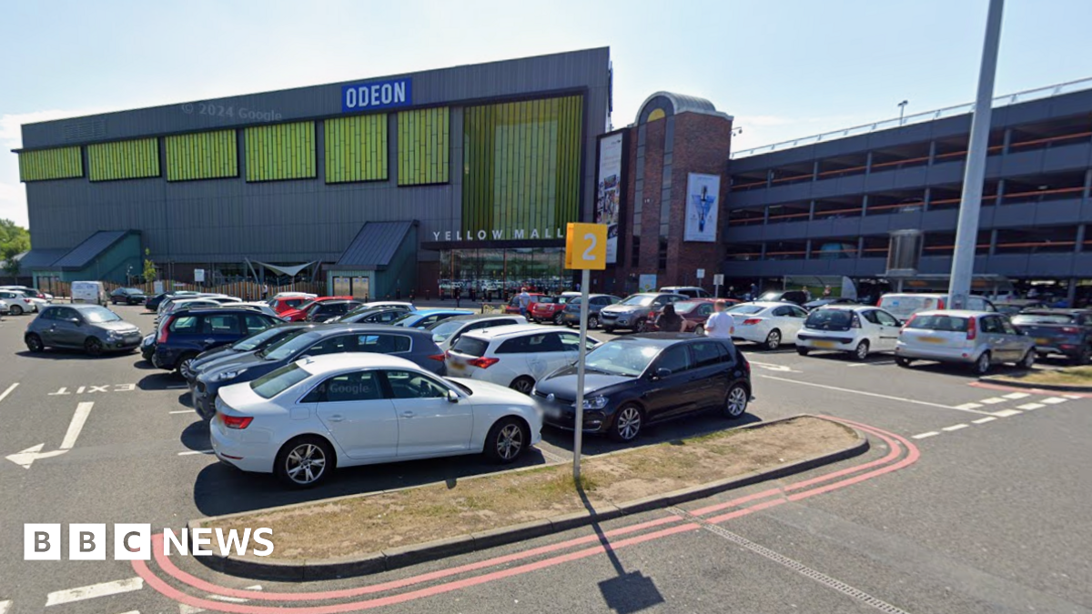Cars parked in a car park. A building is behind it with the words Odeon and yellow mall. A car park building is to the right.