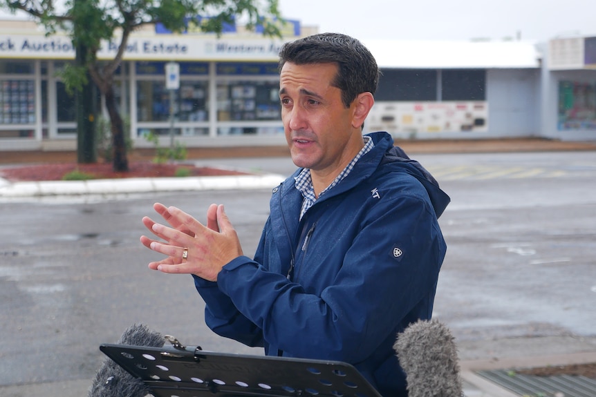 premier david crisafulli in a raincoat speaking on a rainy street