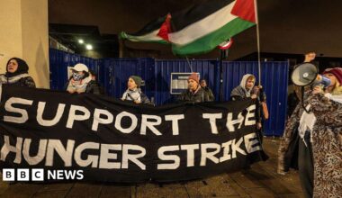 Protesters hold up a sign reading 'Support the hunger strike' and wave Palestine flags