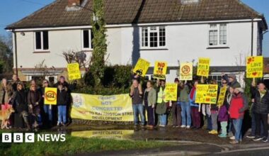 A group of people holding up placards and signs opposing a housing proposal on the edge of a village.
