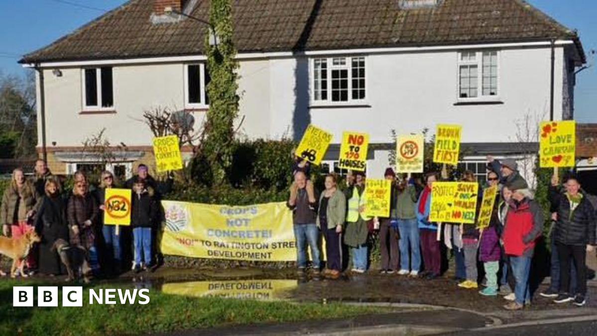 A group of people holding up placards and signs opposing a housing proposal on the edge of a village.