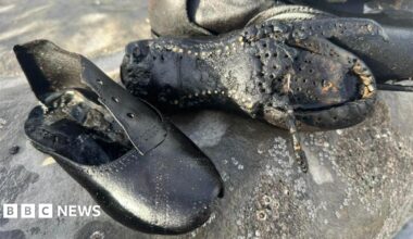 Two black leather boots are on a rock covered in barnacles. The laces are missing. The damaged sole of one of the boots can be seen, along with nails.