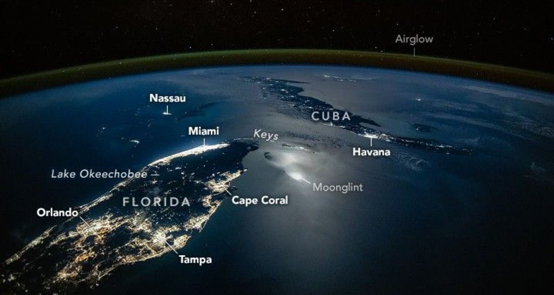A photograph of the tip of Florida and nearby Cuba from space, with lights from cities illuminating the surface of the planet, labeled cities like Orlando and Tampa are seen as well as a green surface over Earth's labeled airglow
