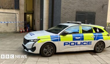 A Suffolk Police car parked in front of a building with blue and white police tape in front of it.