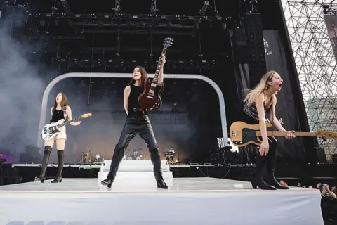 Getty Images Haim play the Primavera festival. Danielle has her guitar raised to the sky, while Este is crouched down and shouting into the audience