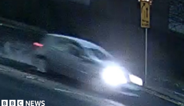 A blurred picture of a car, with its headlights on, driving down a road.