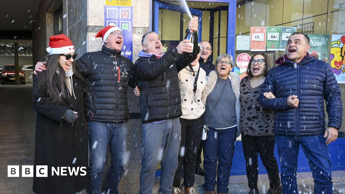 People celebrate winning the first prize of El Gordo Lottery, 79,432, in the town of La Baneza. They are spraying champagne everywhere and smiling. Some are wearing santa hats.