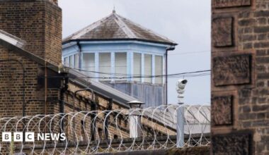 A security camera and barbed wire outside HMP Wandsworth prison in London.