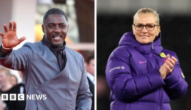 Two individuals shown side by side in separate frames. Idris Elba is wearing a grey suit jacket with a diagonal wrap design and is raising one hand to wave. Sarina Wiegman is wearing a thick purple sports jacket with visible England logos while clapping her hands together.