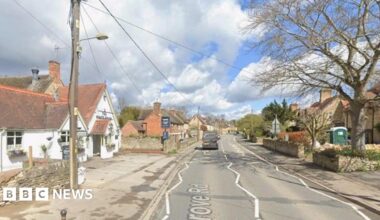 Road through a village with a white pub on the left and homes to the right.