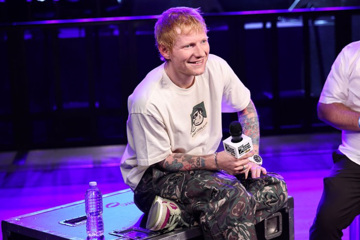 Ed Sheeran performing on stage with a guitar, passionately singing to a large audience at a music event.
