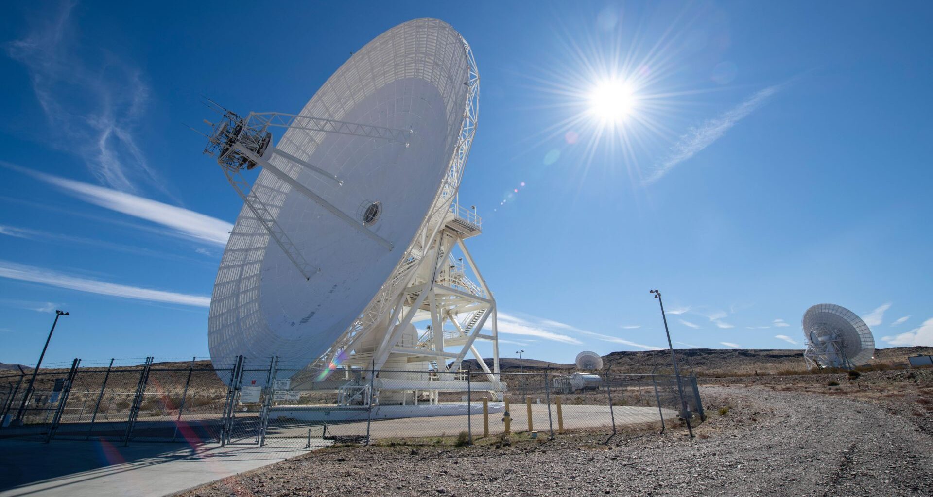 A large white antenna dish points to the left of the screen with the sun in the blue sky behind it