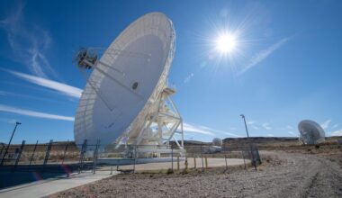 A large white antenna dish points to the left of the screen with the sun in the blue sky behind it