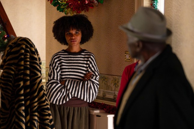 Patrick looks over his shoulder at Jasmine who is stood down the hall with her arms folded in EastEnders