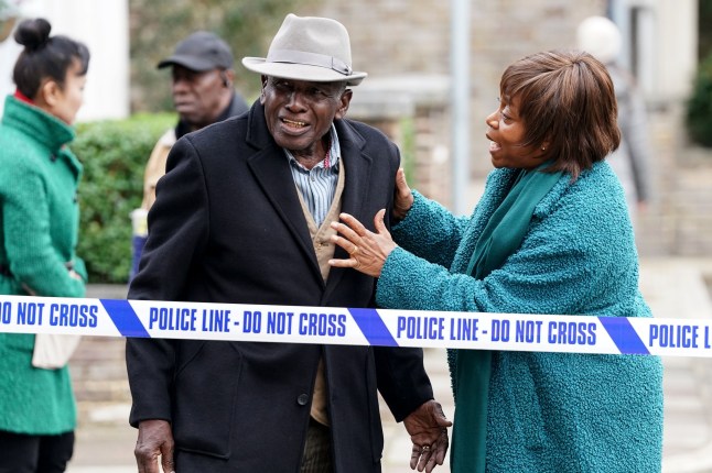 Yolande comforts Patrick as they stand behind police tape on the Square in EastEnders