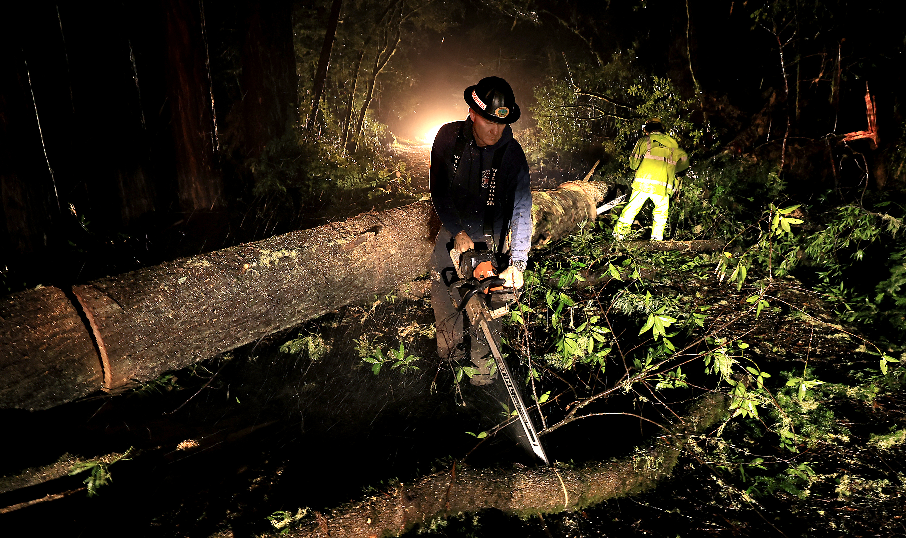 Occidental Volunteer Fire Department personnel begin to chainsaw numerous large...