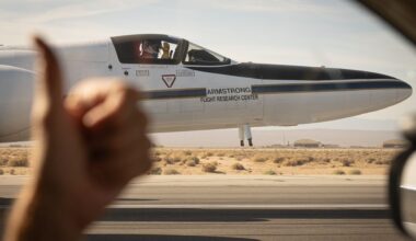 A view from the driver's side window of a car shows a white plane on the runway where the driver's hand shows a thumbs up on the left side of the image.