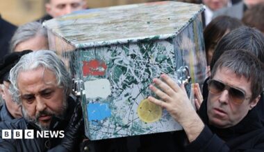 Mani playing bass on stage, wearing a red jacket