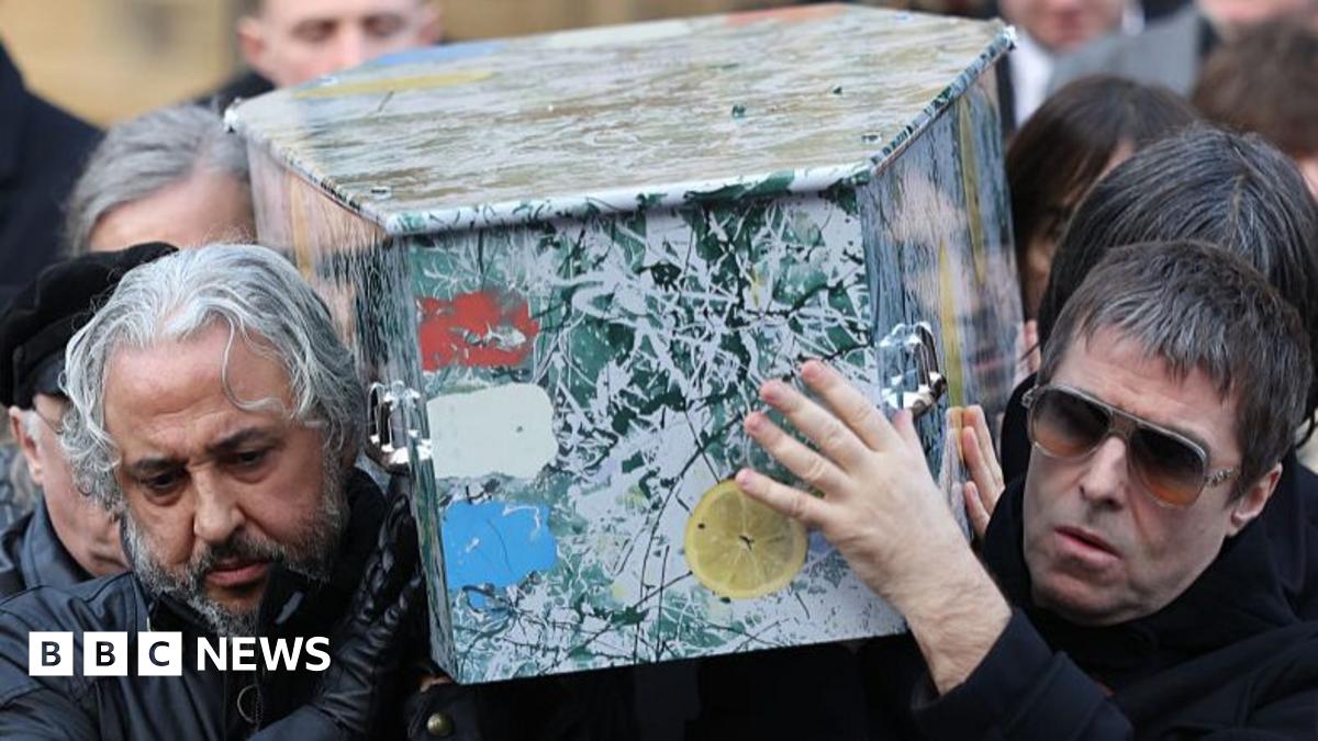 Mani playing bass on stage, wearing a red jacket