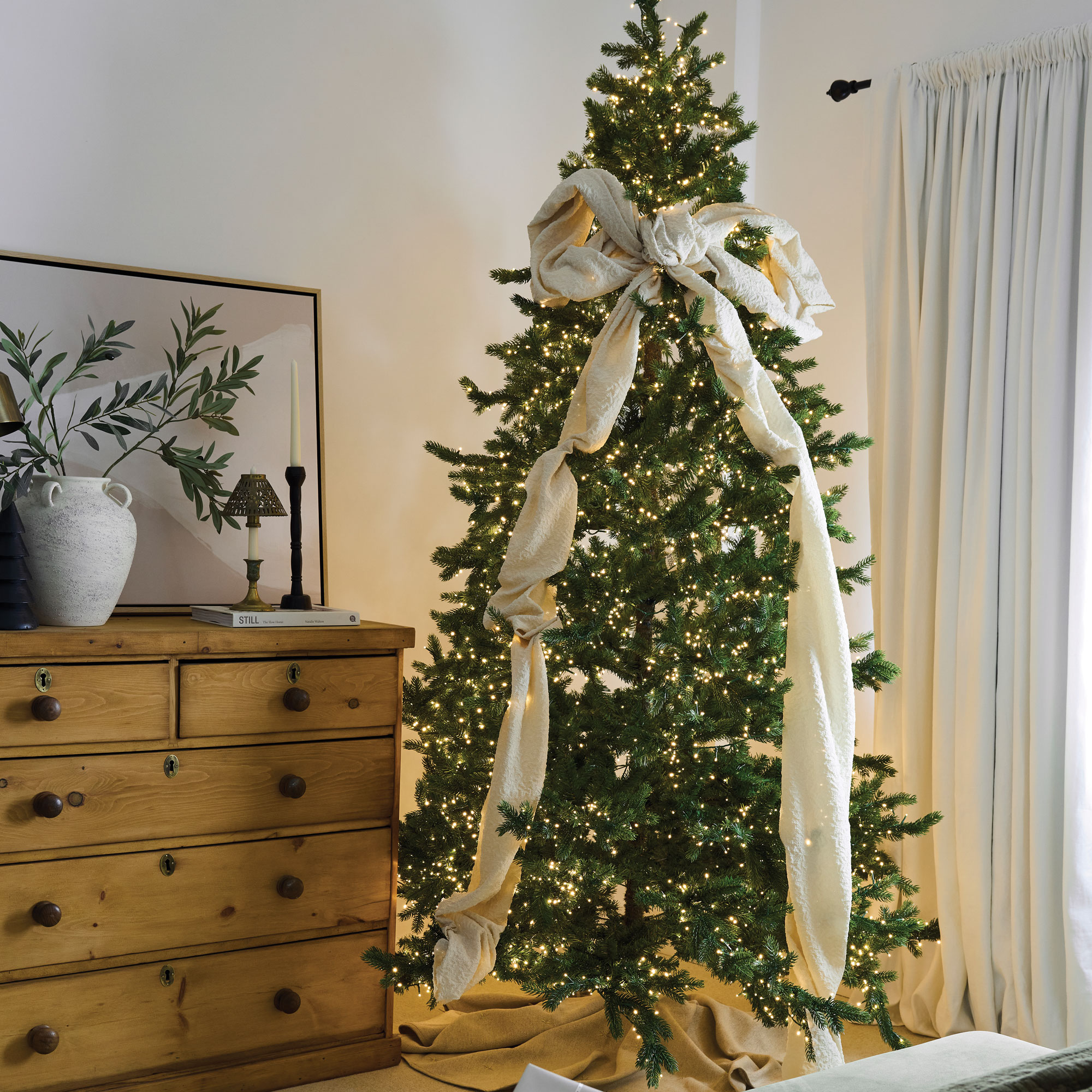 Christmas tree in a bedroom decorated with lights and a large fabric bow