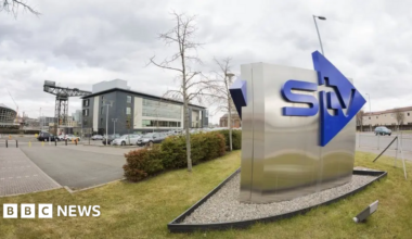 An STV sign outside the HQ building in Glasgow with the Finnieston Crane and the Hydro in the background
