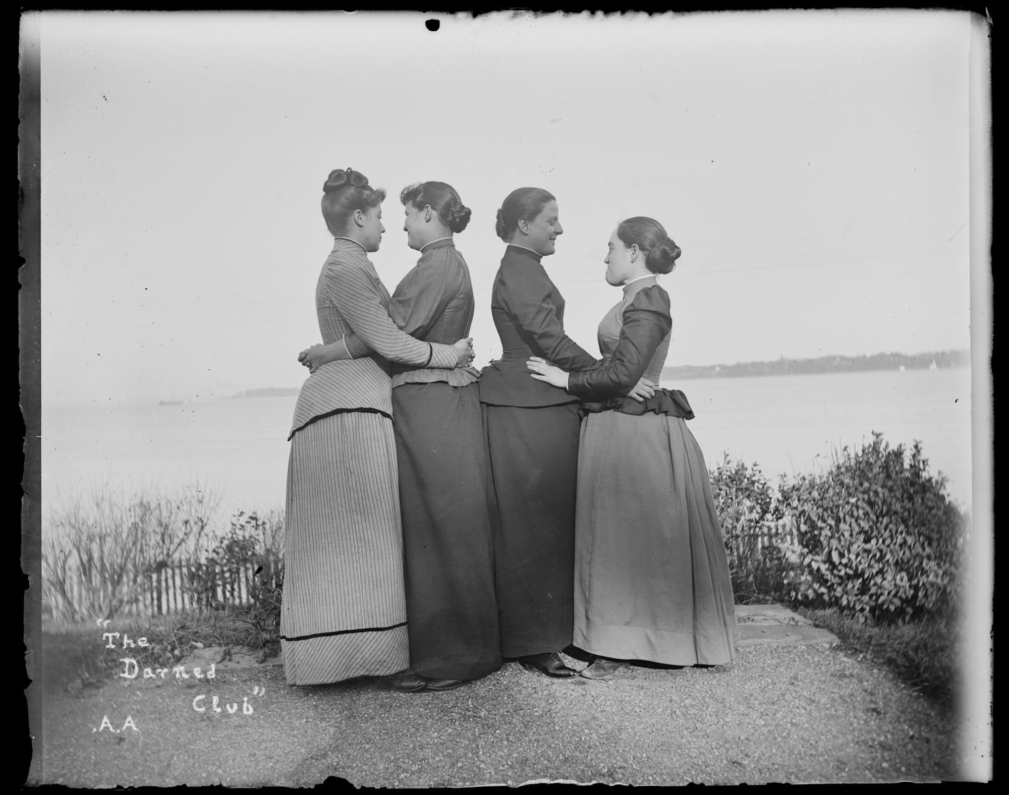 a black-and-white photo from the late 19th century of four women, turned to each other in twos and embracing