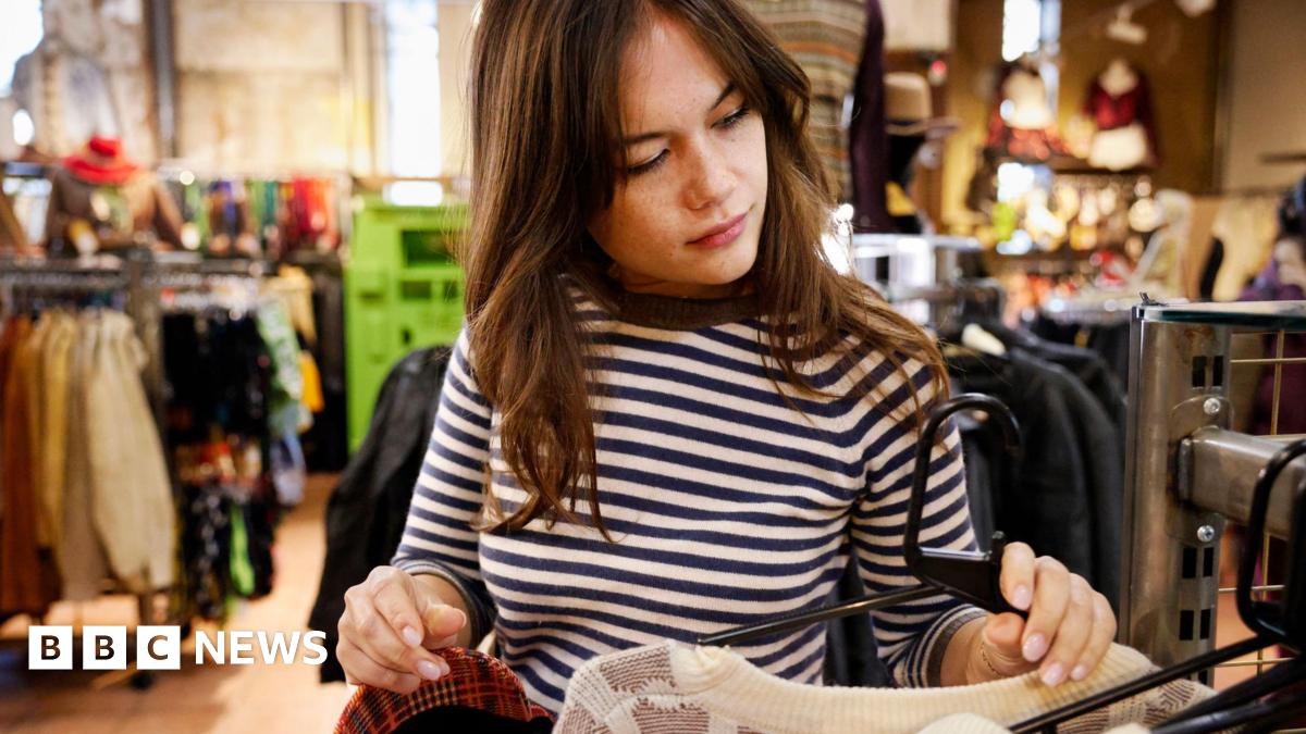 A woman with long brown hair picks up items of clothing of the rack