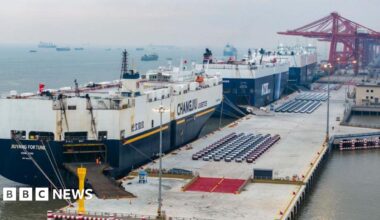 A wide-shot of large ships loading vehicles for export at a port in China