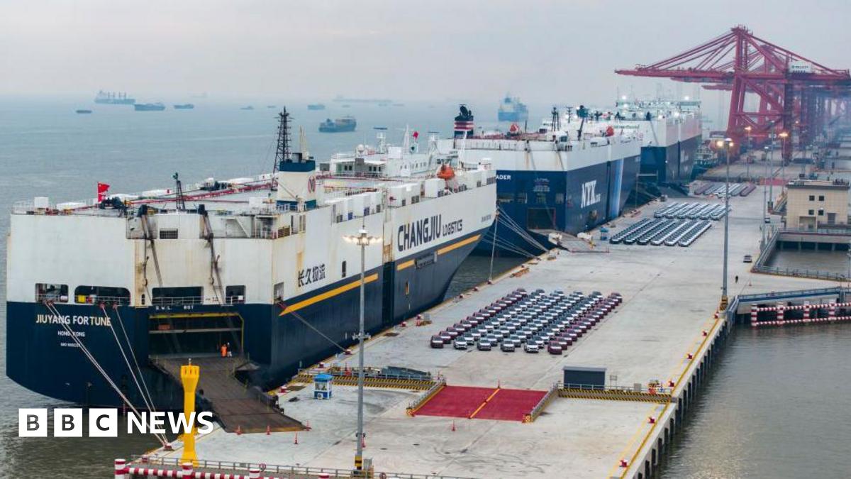 A wide-shot of large ships loading vehicles for export at a port in China