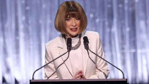 Getty Images Dame Anna Wintour in white dress and jacket, wearing a chunky necklace and sporting a sharp bob