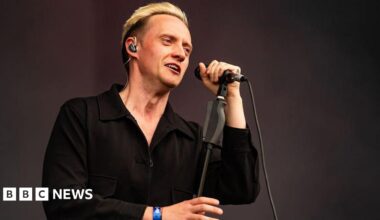 A man with blond hair, standing onstage with a microphone