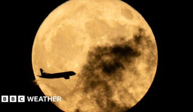 A plane flies in front of the full Moon