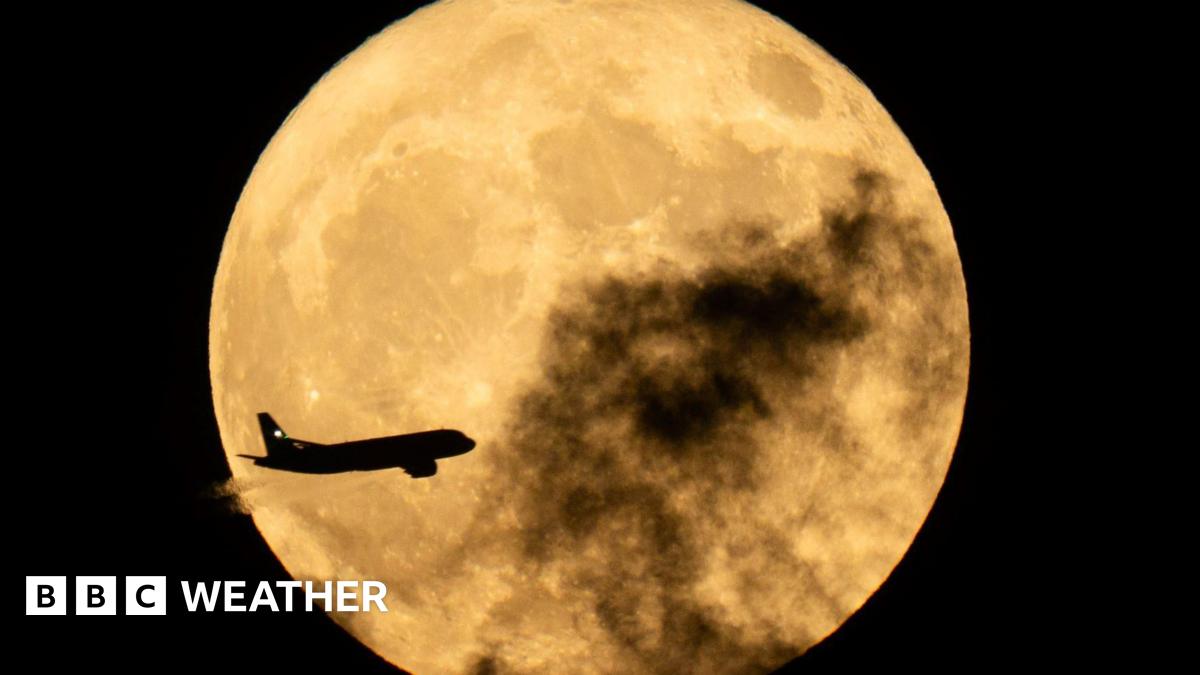 A plane flies in front of the full Moon